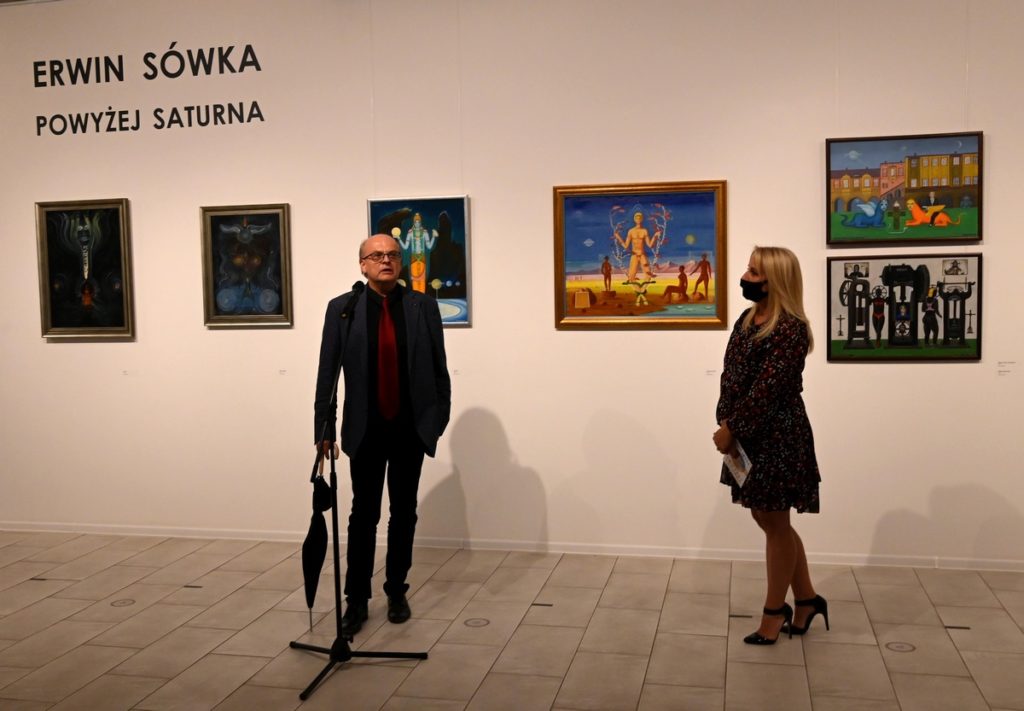wnętrze galerii, na tle obrazów stoją Alicja Wasilewska i Maciej Balcerak (przy mikrofonie)