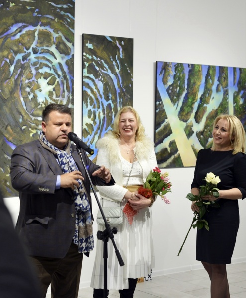 na tle obrazów Romana Fleszara Stoją: przy mikrofonie Piotr Zieliński, obok Ewa Fleszar i Alicja Wasilewska