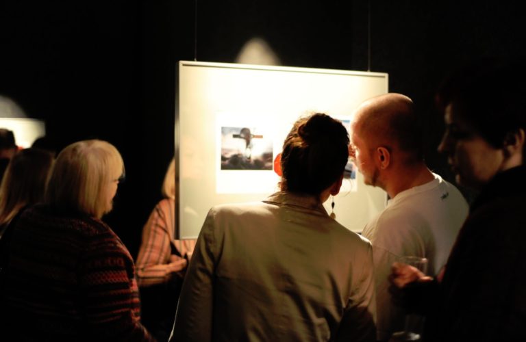 wnętrze Galerii Kreski, trzy osoby oglądają jedna z prezentowanych prac