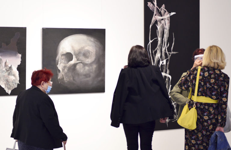 Wnętrze galerii, trzy kobiety w różnym wieku ogładają obrazy, prezentowane na wystawie