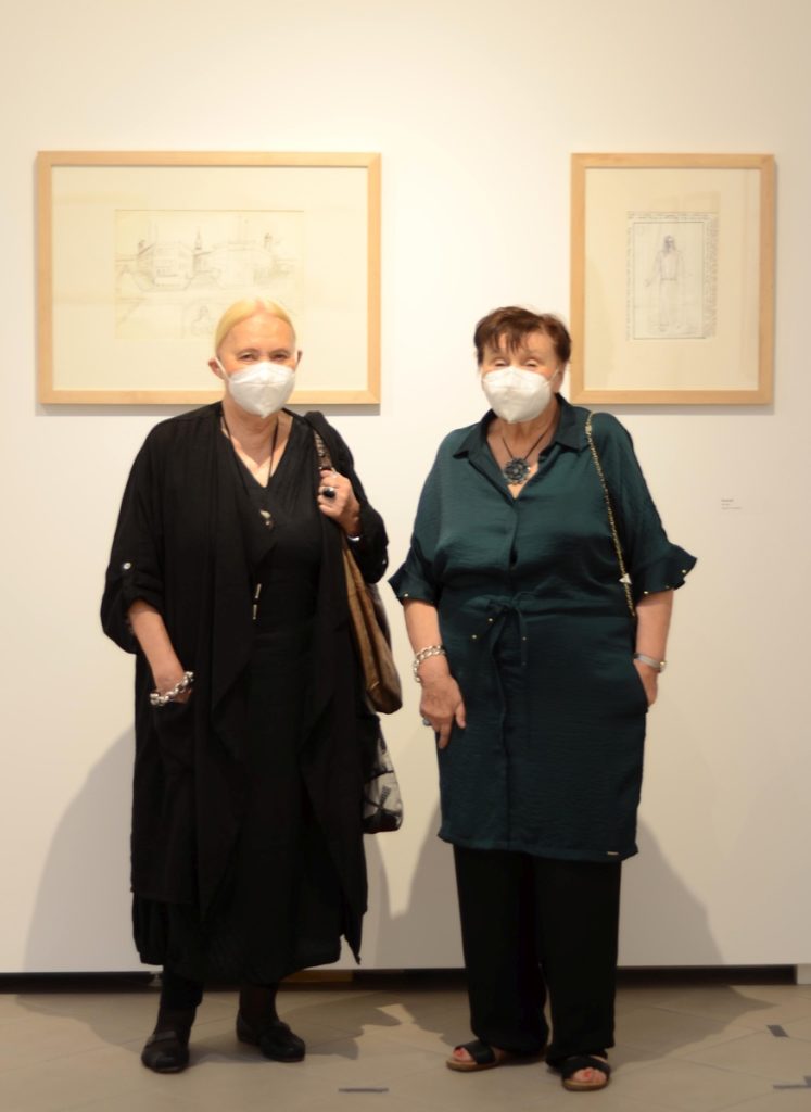 Dwie kobiety w maseczkach na twarzy pozują do zdjęcia, w tle prace Erwina Sówki