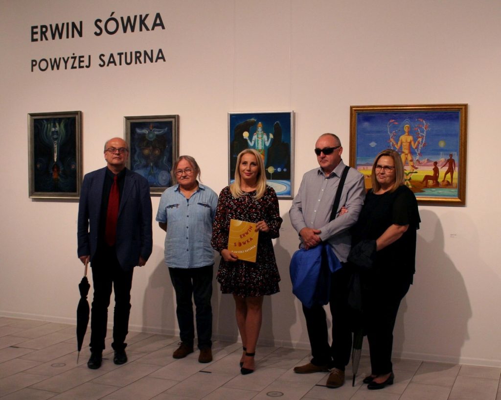 wnętrze galerii, pięc osób, wśród nich Alicja Wasilewska, pozuje do zdjęcia na tle obrazów Erwina Sówki, nad nimi na ścianie tekst:  Erwin Sówka Powyżej Saturna