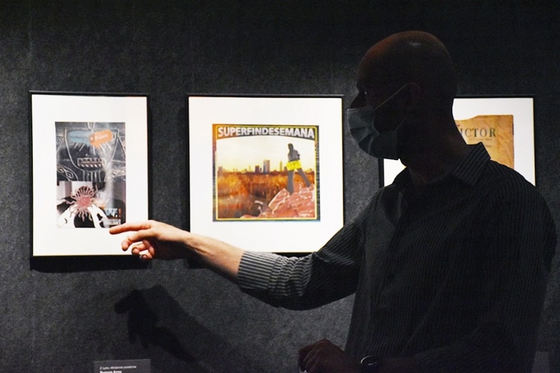 wnętrze galerii, Grzegorz Kozera  wskazuje na jedną ze swoich prac, na twarzy ma maseczkę