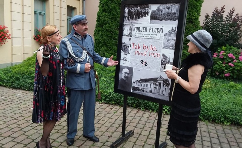 dwie kobiety w strojach z lat dwudziestych i mężczyzna przebtany za marszałka Pilsudskiego stoją przy jednej z plansz wystawy