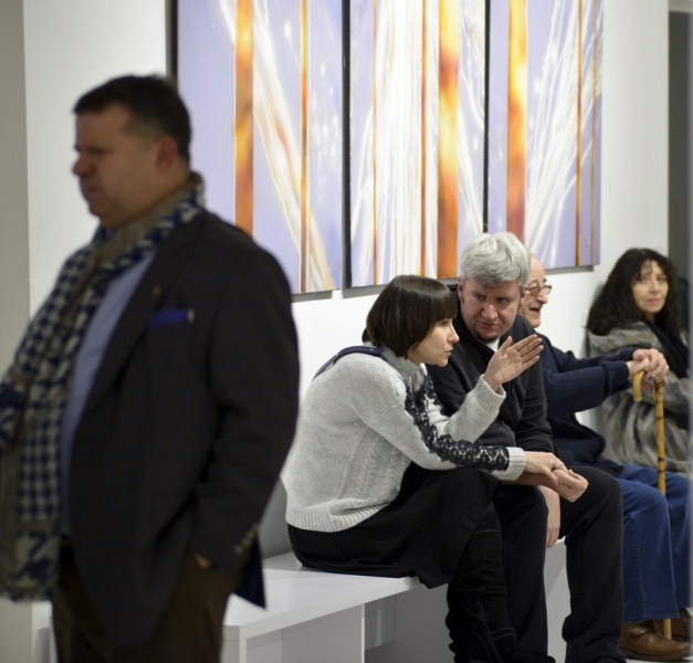 zdjęcie z wystawy, na planie pierwszym Piotr Zieliński, w tle kobieta i mężczyzna siedzą na ławeczce i rozmawiają