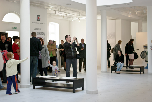 wnętrze galerii, ponad dwadzieścia osób ogląda wystawę Dostrzeżeni