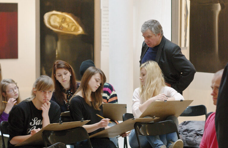 Wnętrze Galerii. Grupa młodych osób siedzi na krzesłach i rysuje