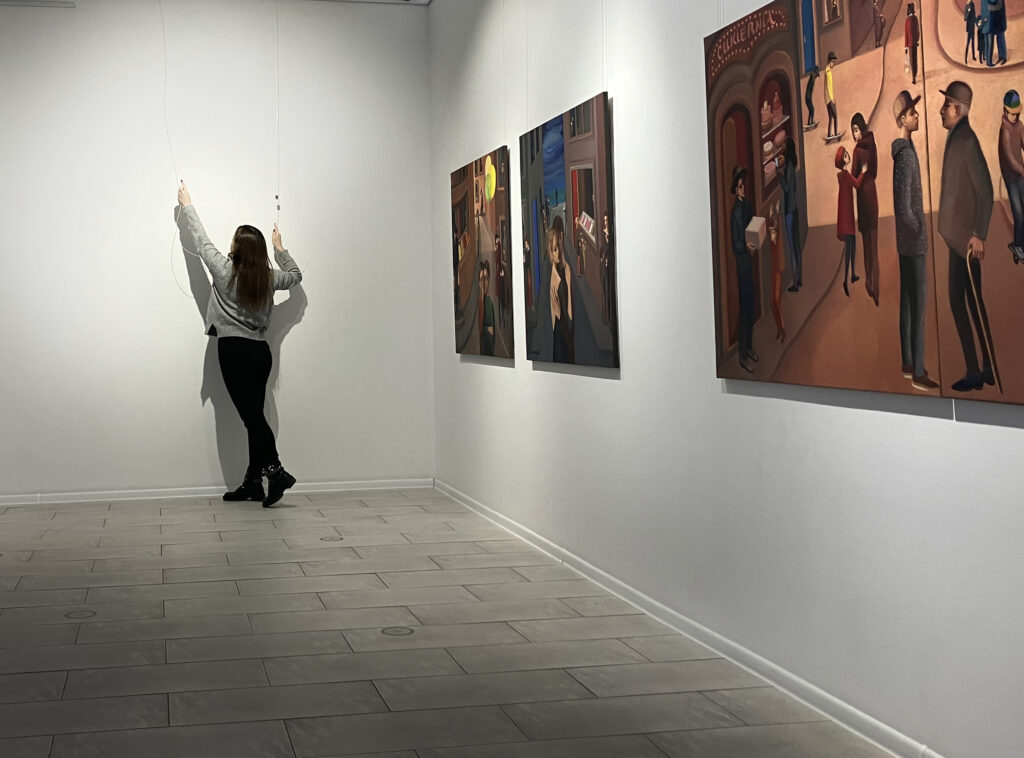 wnętrze galerii po prawej stronie wiszą trzy obrazy Katarzyny Karpowicz, a na wprost przy ścianie stoi dziewczyna